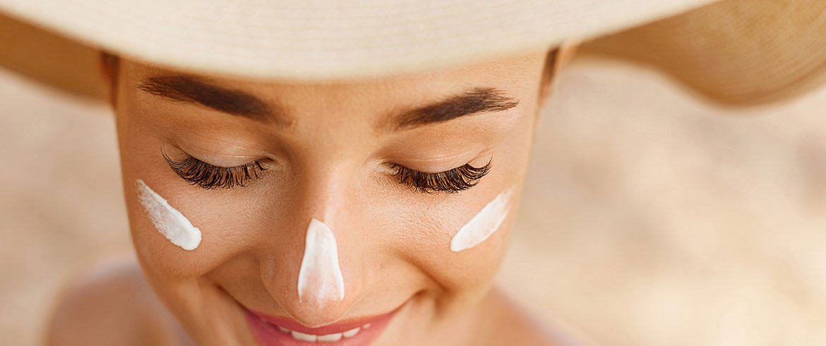 Frau mit Sonnencreme auf Nase und Wangen, lächelt mit einem Sonnenhut, zeigt die Anwendung von Sonnencreme im Gesicht und die Bedeutung der Haltbarkeit.